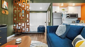 Un ambiente compatto con angolo cottura, divano, letto e un pannello decorativo in legno.