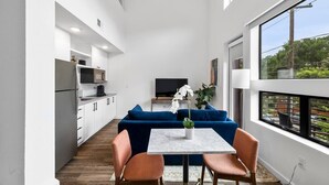 A modern kitchen with white cabinets, a blue sofa, and a dining table with chairs. - Charming DT ATX Loft | Near Rainey St (Austin)