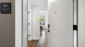 A hallway with a wooden floor, white walls, and a door with a number sign. - Charming DT ATX Loft | Near Rainey St (Austin)