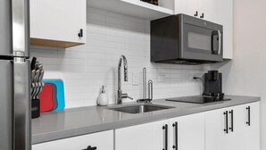 A modern kitchen with white cabinets, stainless steel appliances, and a black microwave. - Charming DT ATX Loft | Near Rainey St (Austin)