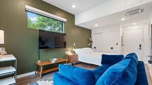 A modern room with a bed, blue sofa, wooden side table, and a TV mounted on the wall.