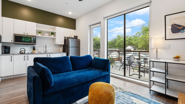 A modern kitchen with white cabinets, a blue sofa, and a large window overlooking a balcony.