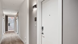 A hotel hallway with a wooden floor, a door with a keypad lock, and an exit sign.