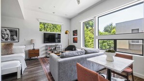 A modern living room with a sofa, a TV, a dining table, and large windows. - Bright Studio Near Rainey St / Mins to DT ATX (Austin)