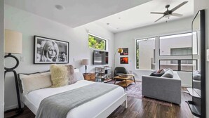 A modern hotel room with a bed, a sofa, a TV, a desk, and large windows. - Bright Studio Near Rainey St / Mins to DT ATX (Austin)