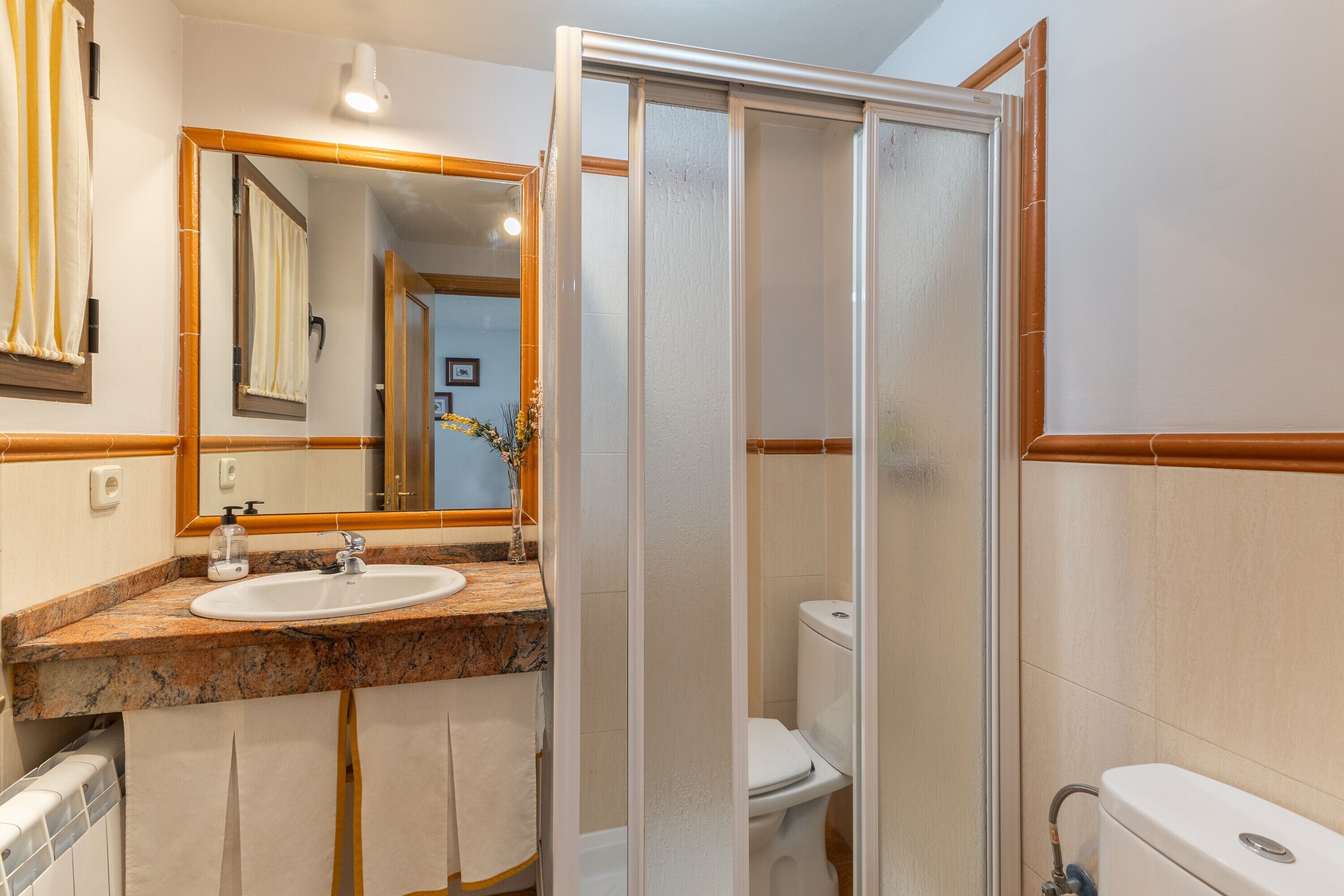 A bathroom with a sink, mirror, toilet, and shower enclosure.