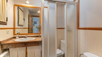 A bathroom with a sink, mirror, toilet, and shower enclosure.