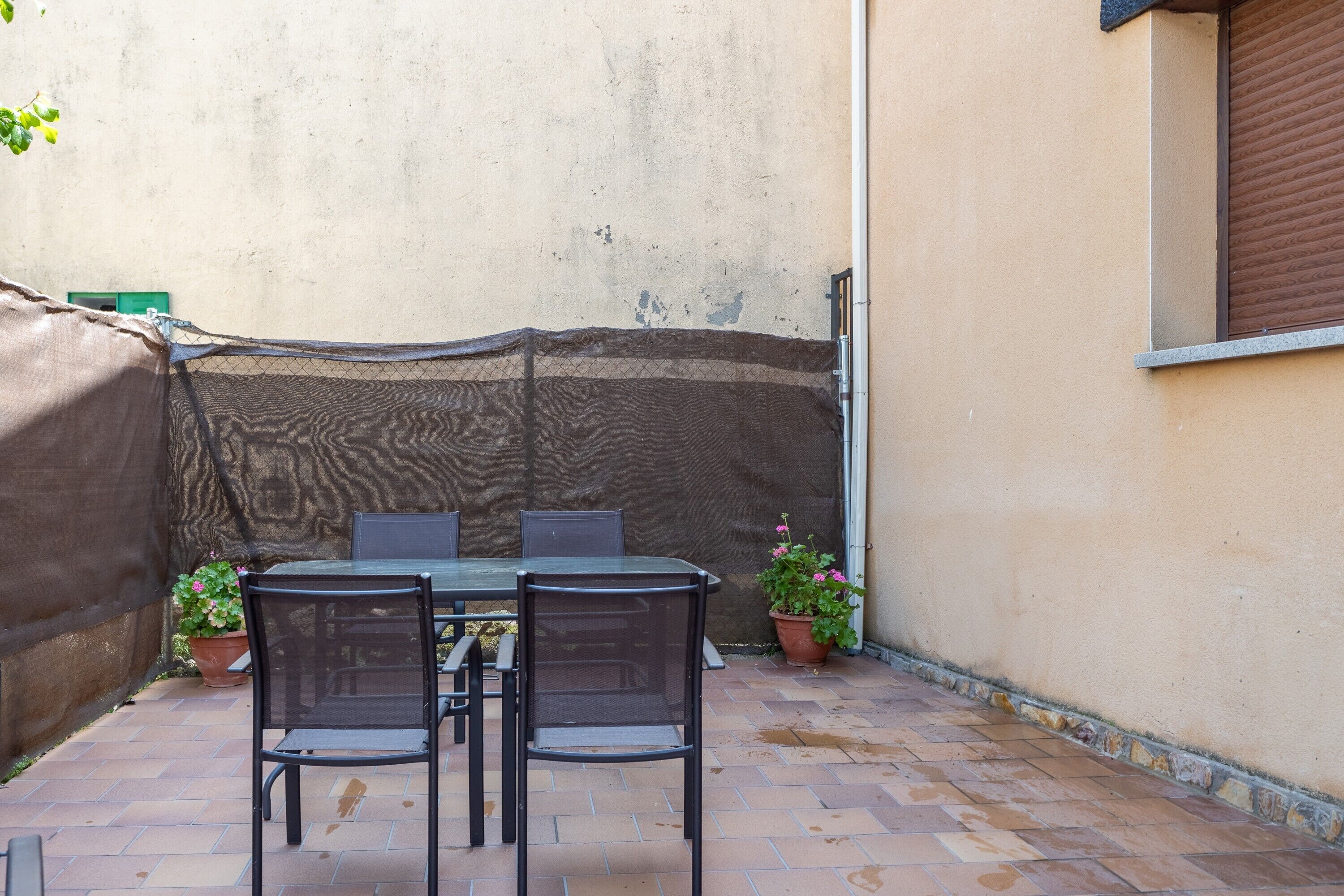 Un patio al aire libre con una mesa, sillas, una zona cubierta y plantas en macetas.