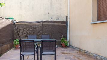 Un patio al aire libre con una mesa, sillas, una zona cubierta y plantas en macetas.