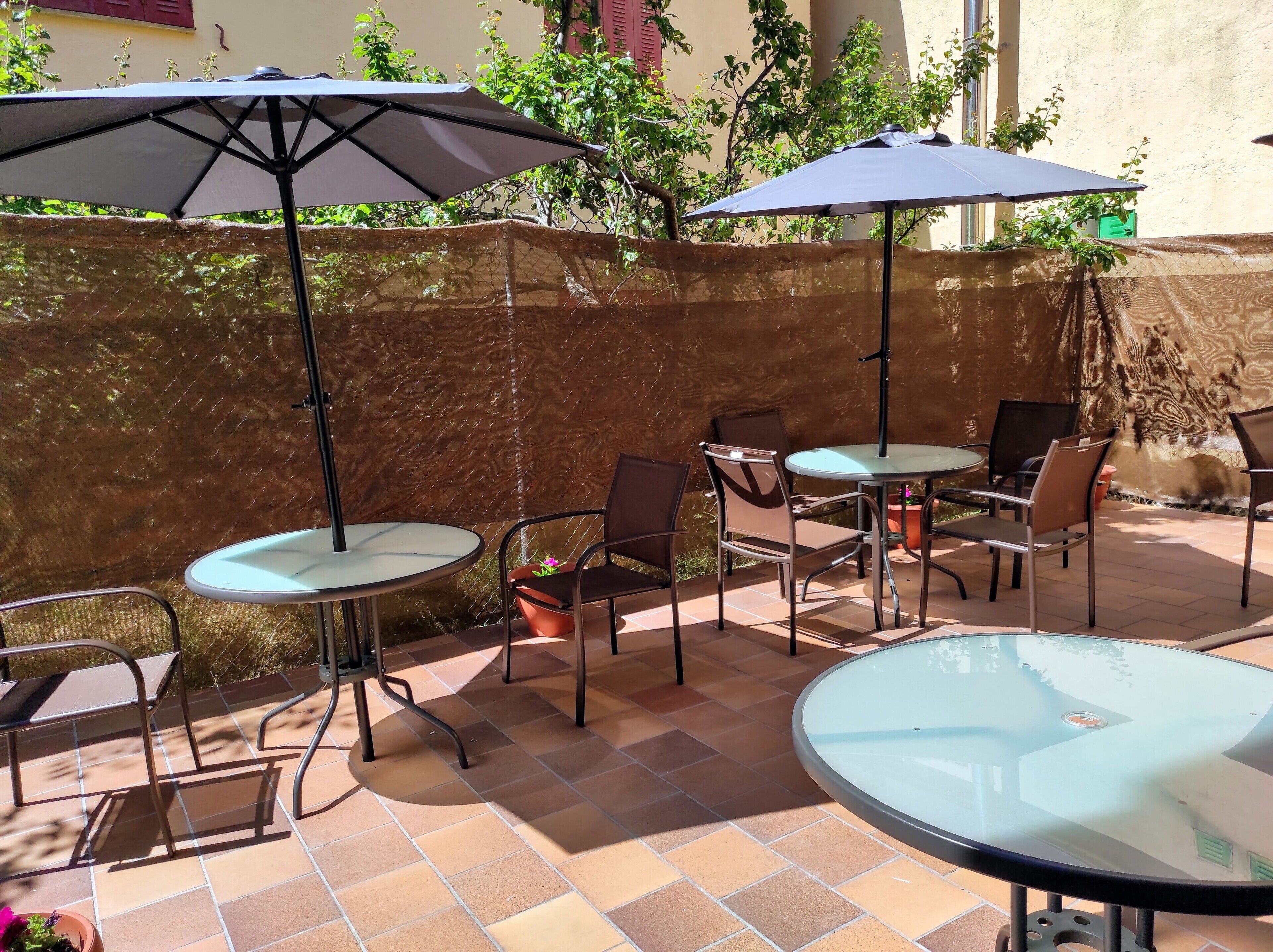 Un patio al aire libre con mesas y sillas redondas, dos sombrillas y un piso de baldosas.