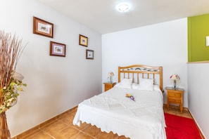 A neatly made bed with a wooden headboard, a bedside table with a lamp, and a vase with flowers on the left side.