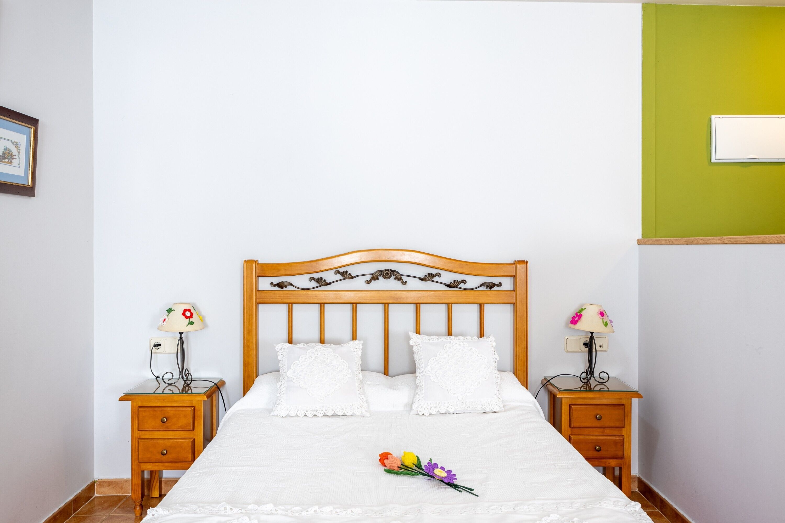 Un llit ben fet amb llençols blancs i dos coixins decoratius, flanquejat per dues taules de nit amb llums, en una habitació amb una paret d'accent verd.
