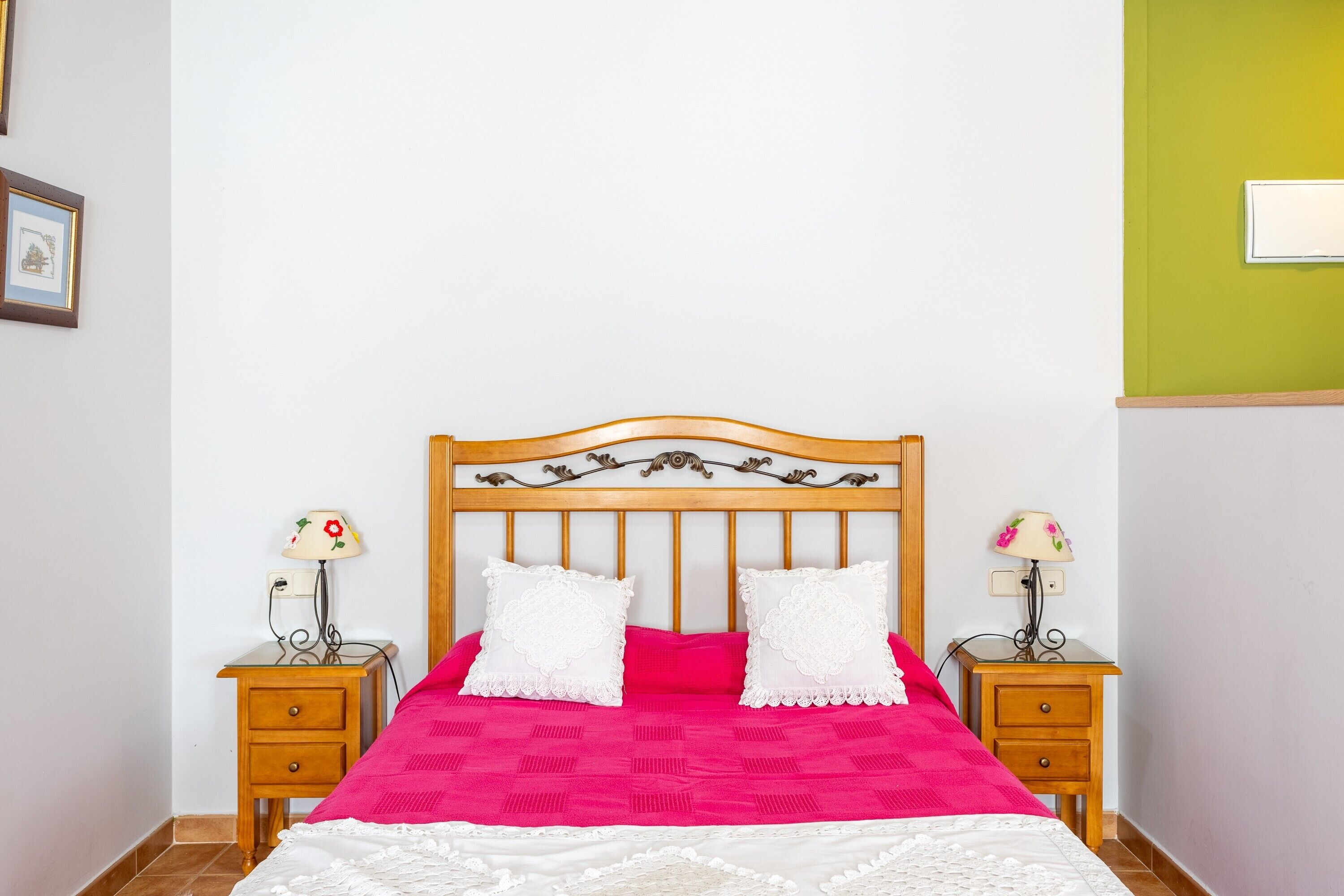 Un lit avec une tête de lit en bois, deux tables de chevet avec des lampes et une couvre-lit rose vif.