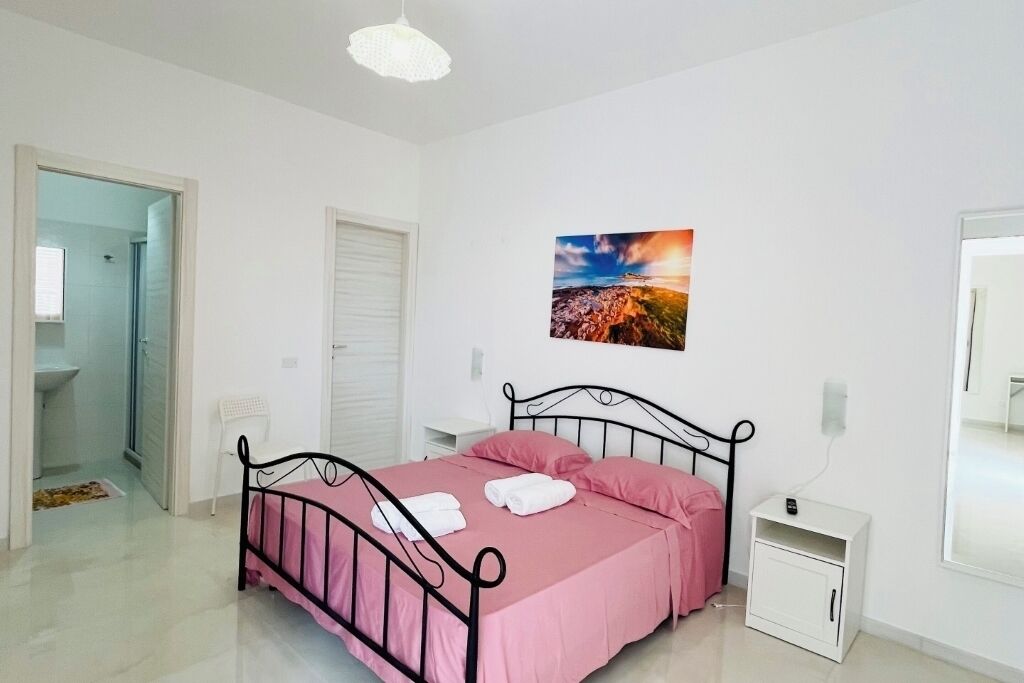 Een slaapkamer met een bed, een nachtkastje, een schilderij en een deur naar een badkamer.