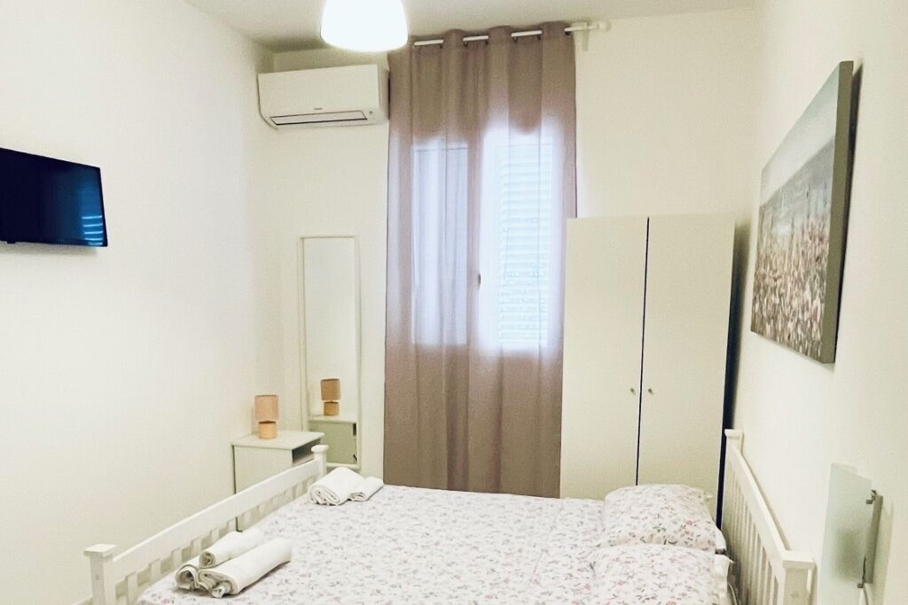Een slaapkamer met een bed, een kledingkast, een spiegel, een nachtkastje en een aan de muur bevestigde televisie.