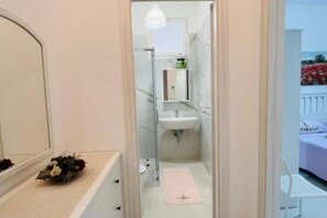 Un baño estrecho con espejo, lavamanos y una pequeña repisa.