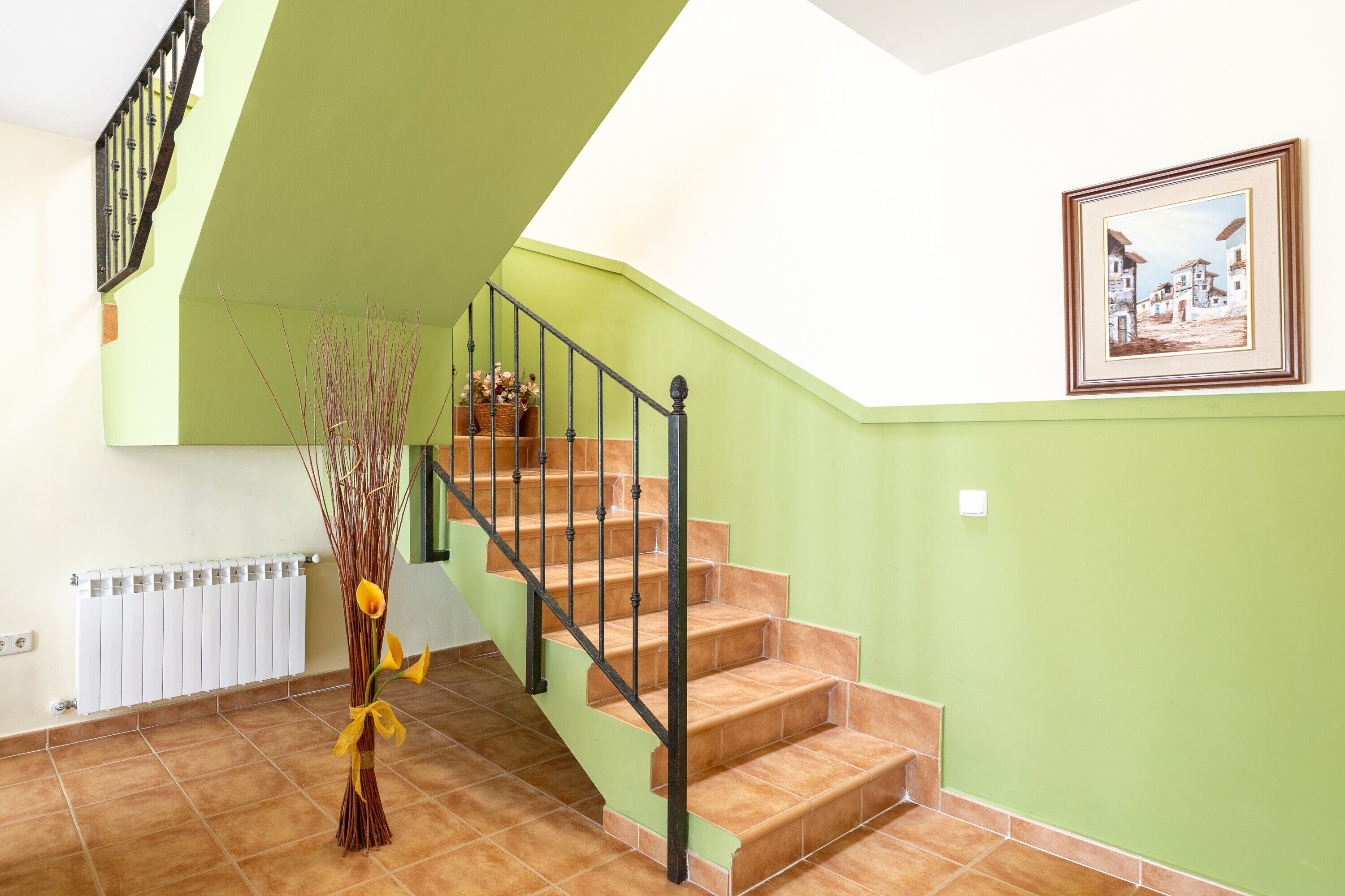 Un escalier avec une rampe noire, un radiateur et un tableau encadré accroché au mur.