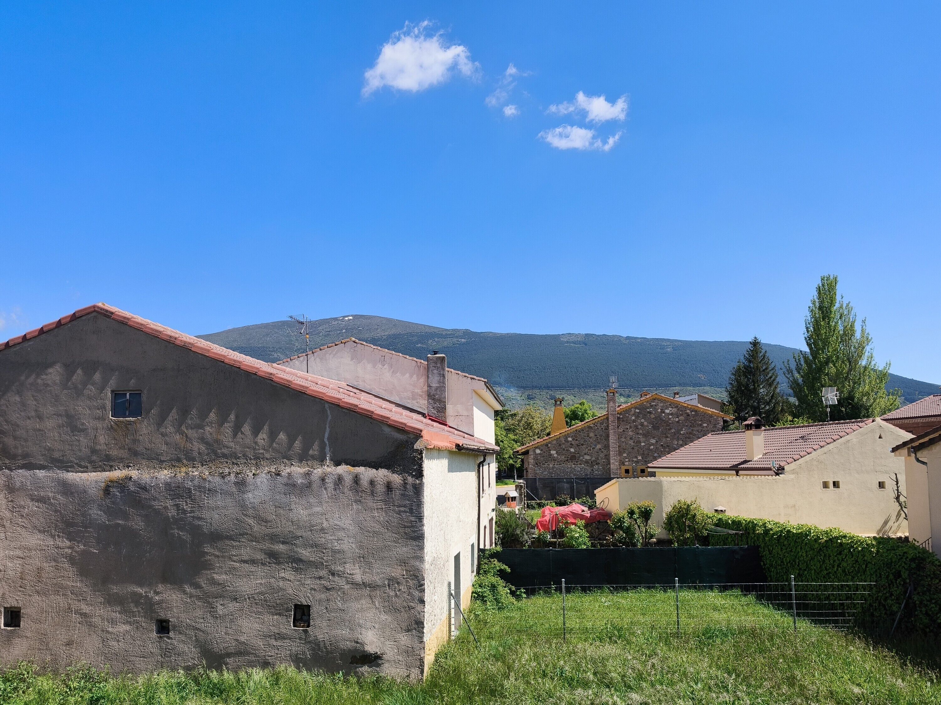 Un borgo rurale con edifici in pietra, cielo sereno e una montagna sullo sfondo.