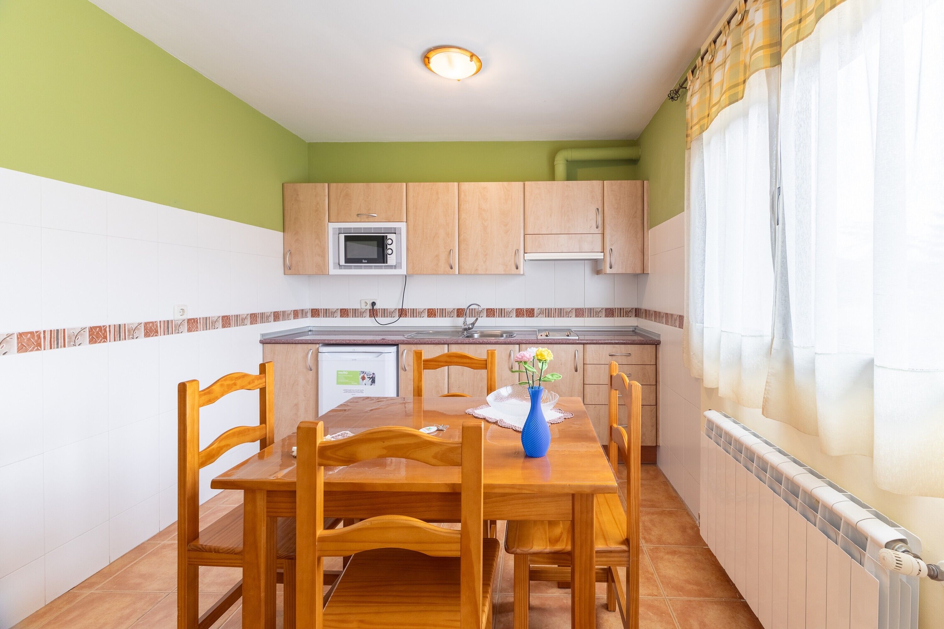 Una cocina compacta con armarios de madera, un microondas y una mesa de comedor con sillas.
