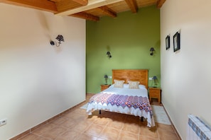 A bedroom with a wooden headboard, a bed with a patterned blanket, two bedside tables with lamps, and a green wall.