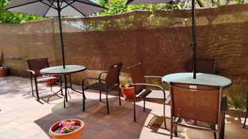 Eine Terrasse im Freien mit zwei runden Tischen, vier Stühlen, zwei Sonnenschirmen und Blumentöpfen.