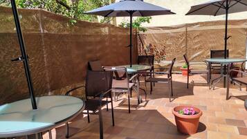 Un área de patio al aire libre con mesas, sillas, sombrillas y plantas en macetas.