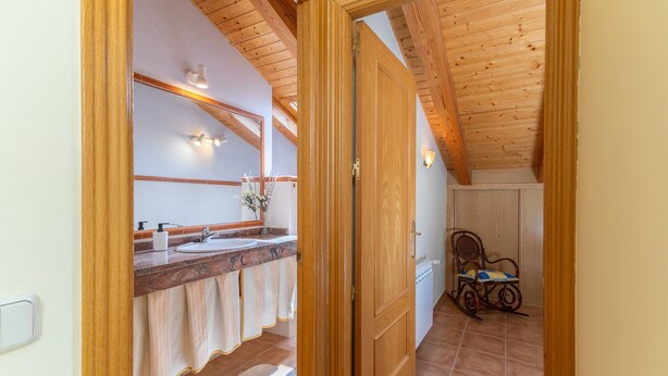 A wooden door leading to a bathroom with a sink, mirror, and towel rack.