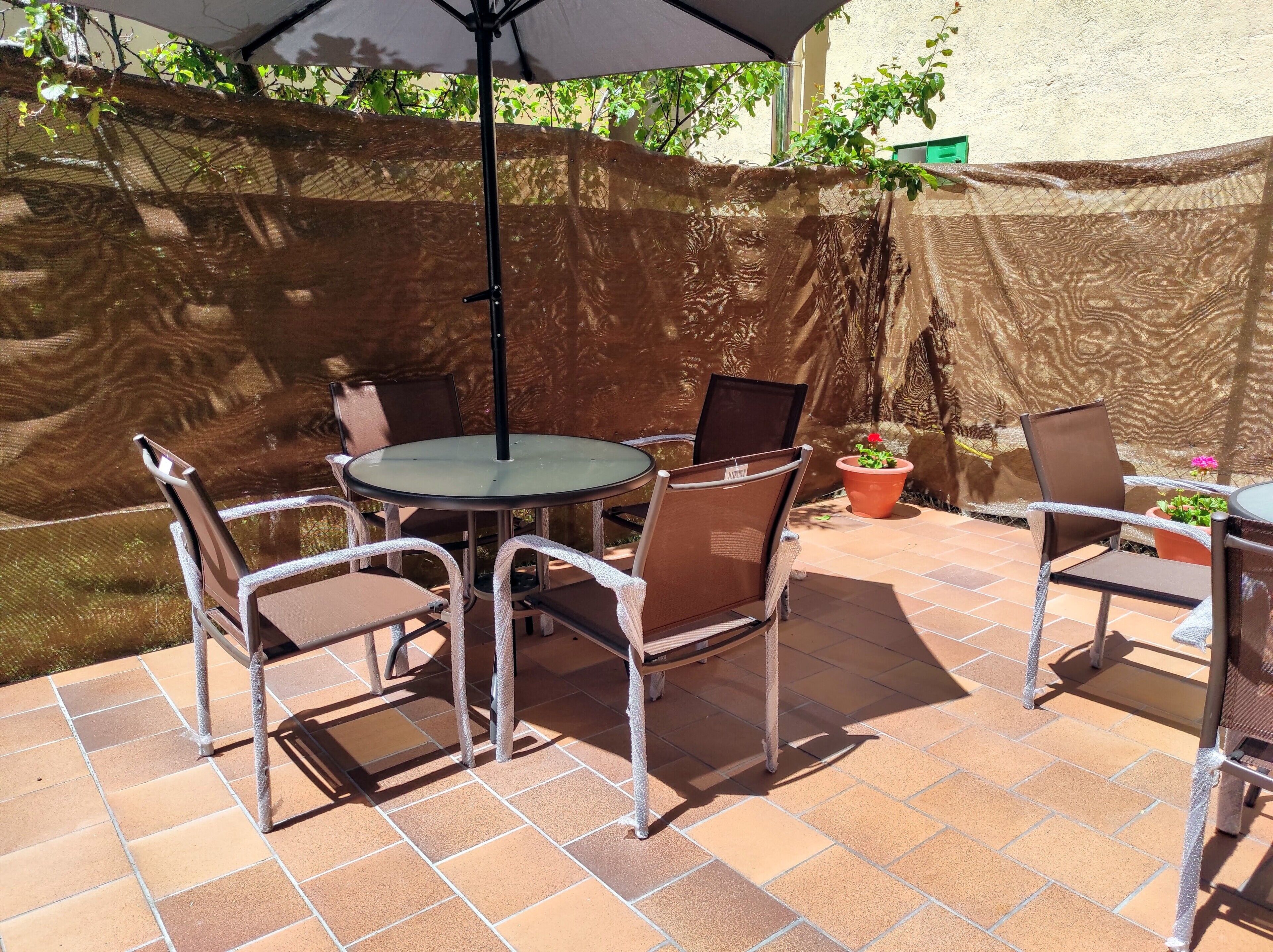 Un patio al aire libre con una mesa redonda y sillas, una sombrilla protectora y una cerca decorativa.