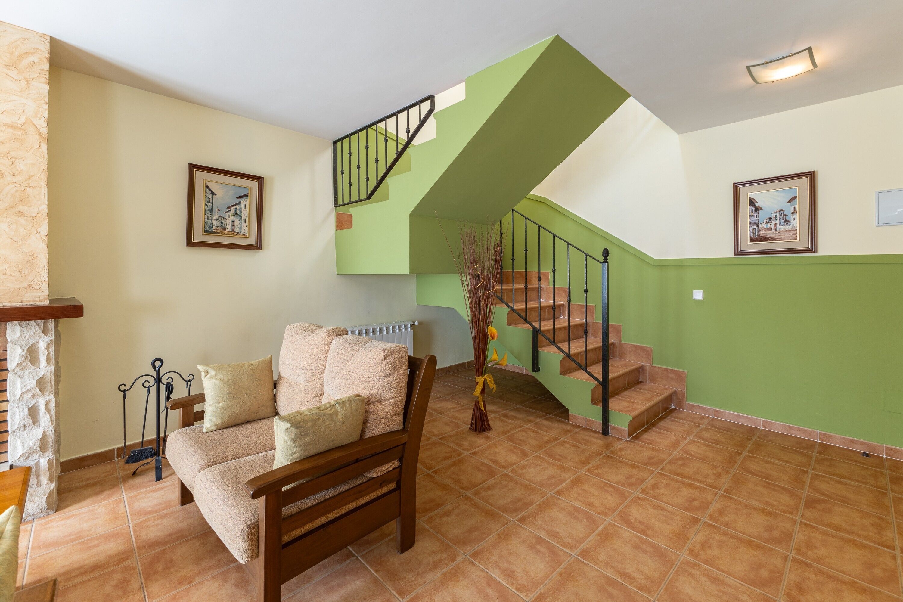 Una sala de estar con un sofá, una silla de madera, una escalera y paredes verdes, además de un radiador.