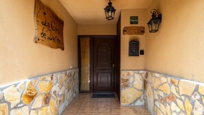 A hallway with a stone-tiled floor, a wooden door, and a sign on the wall.