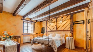 A bedroom with a wooden ceiling, a bed with a hanging swing, a radiator, a window, and a small table with a vase. - Casa La Mora Cantana (Castrojeriz)