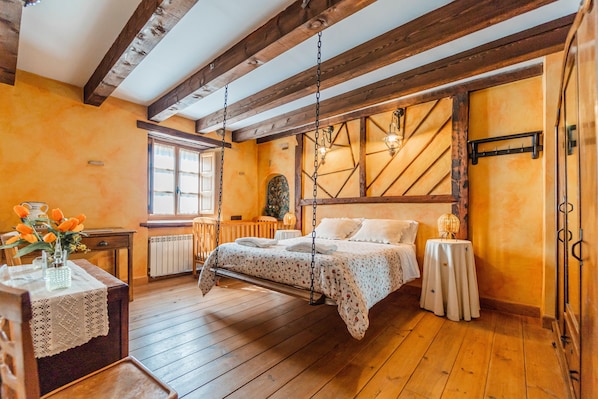 Un dormitorio con techo de madera, una cama con un columpio colgante, un radiador, una ventana y una pequeña mesa con un jarrón.