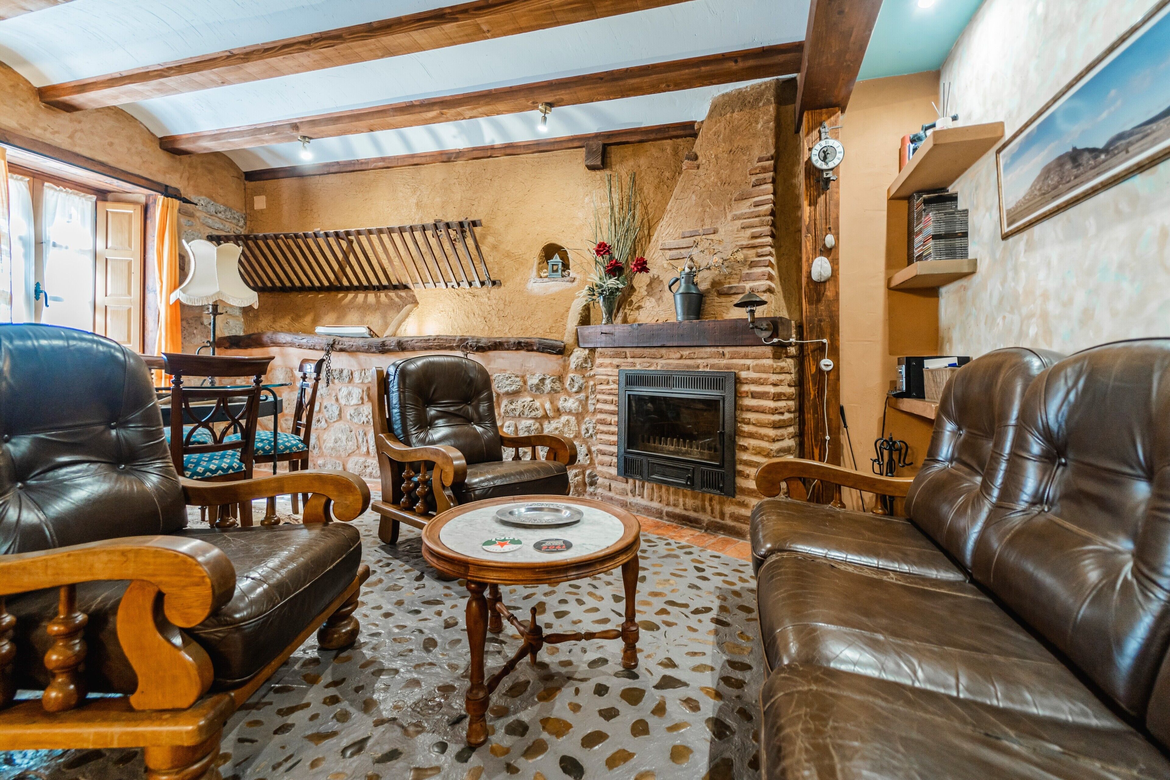 A rustic interior with leather sofas, a stone fireplace, wooden furniture, and a patterned floor.