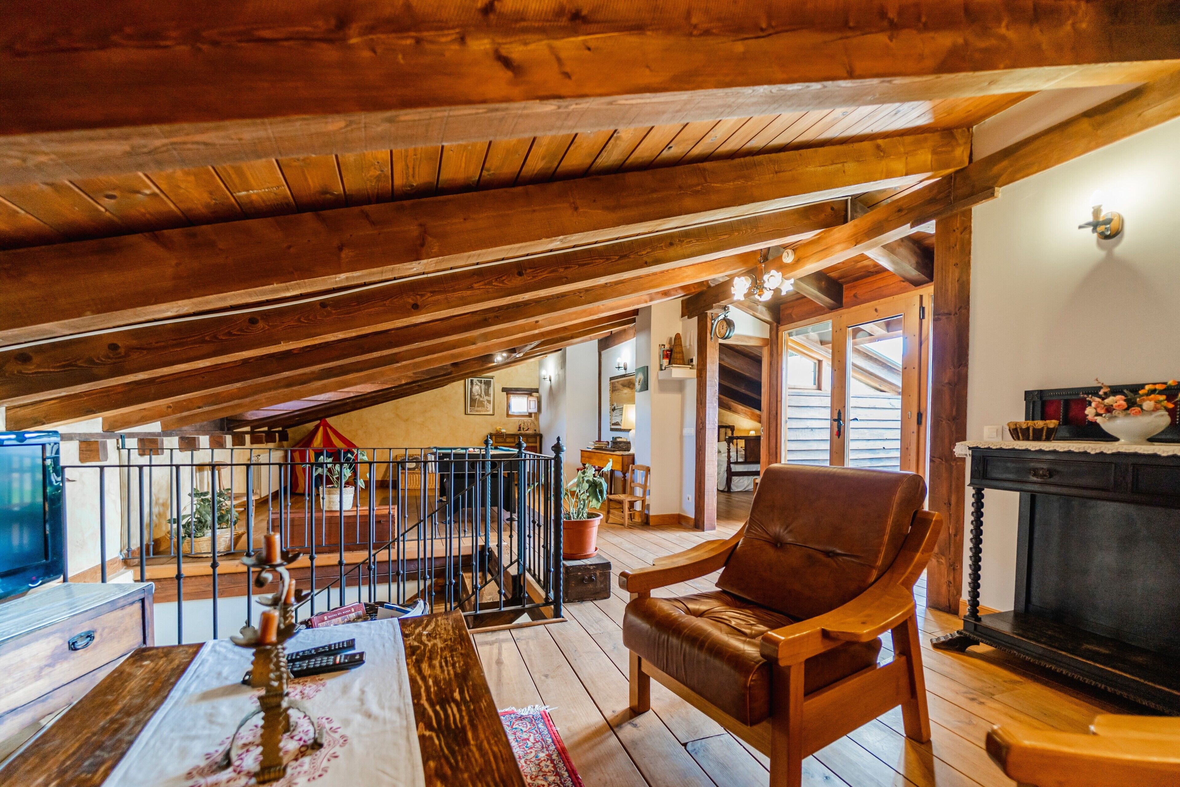 Ein Holzinterieur mit hohen Decken, einem Kamin, einem Ledersessel und einer Treppe, die zu einer weiteren Ebene führt.