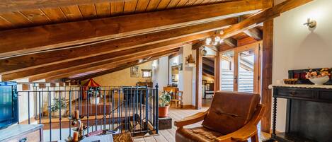 Ein Holzinterieur mit hohen Decken, einem Kamin, einem Ledersessel und einer Treppe, die zu einer weiteren Ebene führt.
