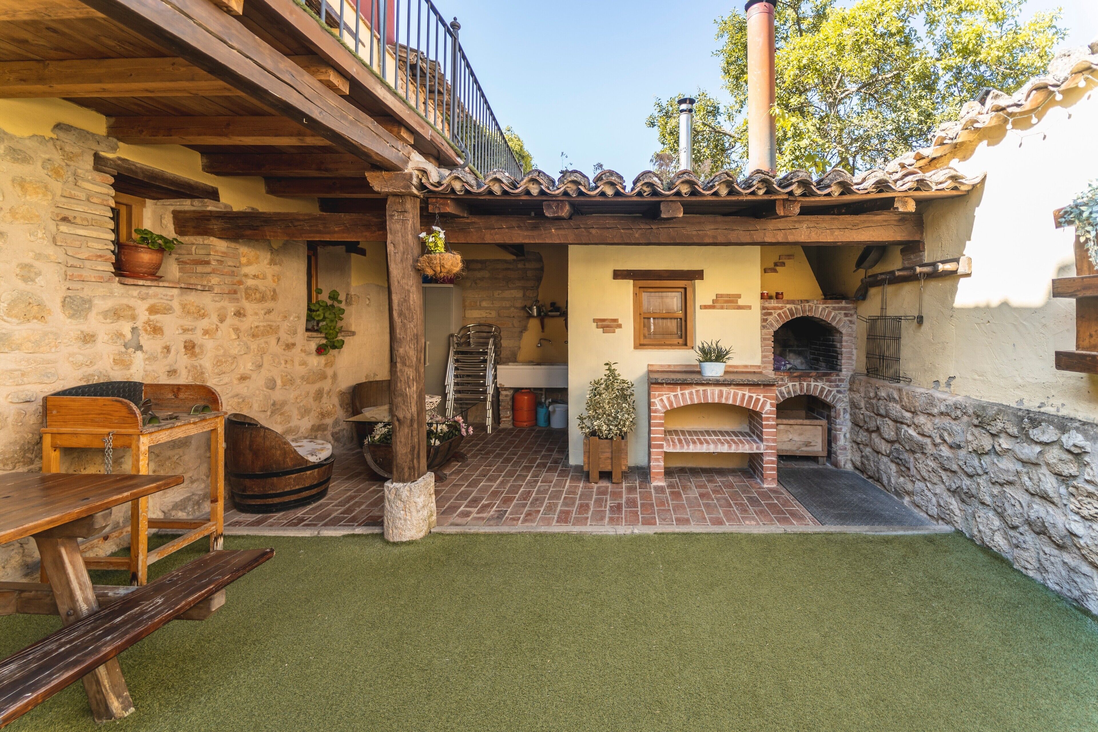A rustic outdoor patio with a brick oven, wooden furniture, and stone walls.