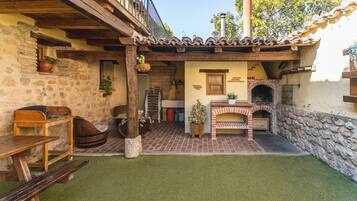 A rustic outdoor patio with a brick oven, wooden furniture, and stone walls.