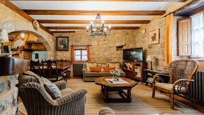 A rustic interior with stone walls, wooden beams, a chandelier, a sofa, a coffee table, and a television. - Casa La Mora Cantana (Castrojeriz)