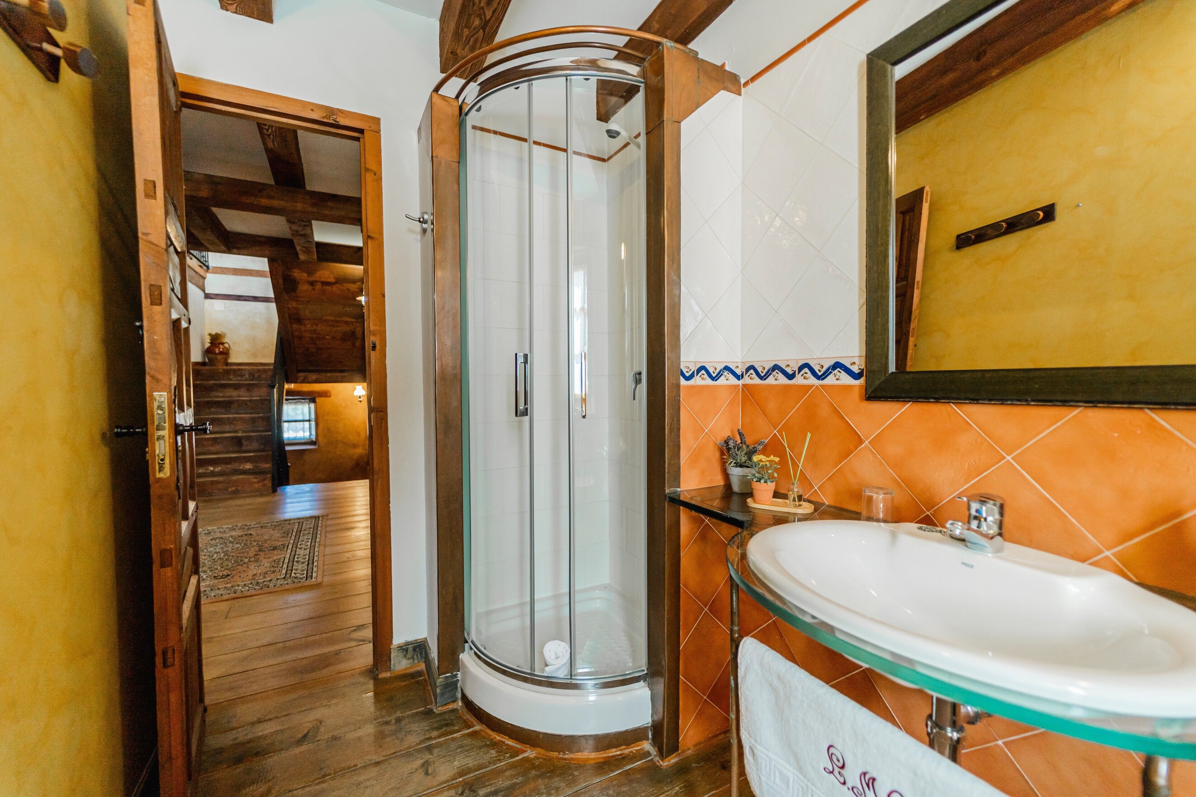 A bathroom with a glass shower enclosure, a sink with a glass basin, and a wooden staircase leading to another room.