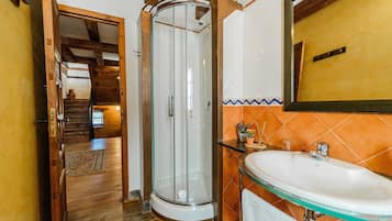 Un baño con cabina de ducha de vidrio, un lavabo con lavamanos de vidrio y una escalera de madera que conduce a otra habitación.