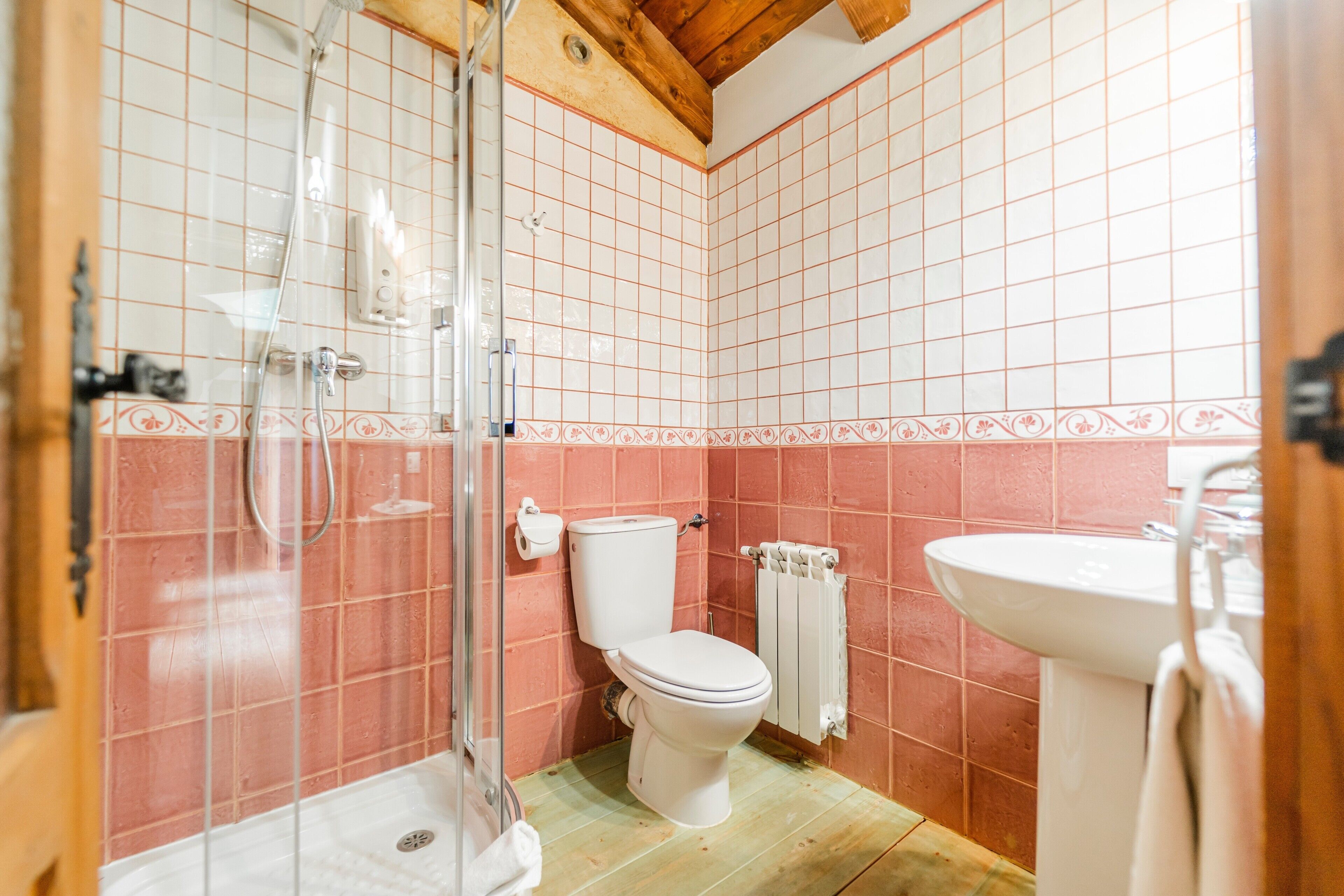 Ein Badezimmer mit Dusche, Toilette und Waschbecken, mit rosa und weißen Fliesen.