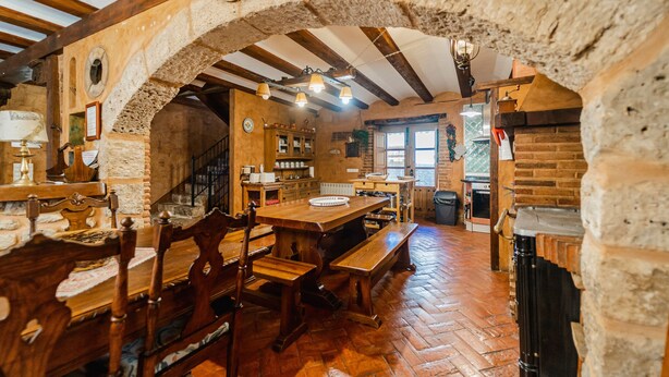 A rustic dining area with stone walls, wooden beams, and a brick fireplace. - Casa La Mora Cantana (Castrojeriz)