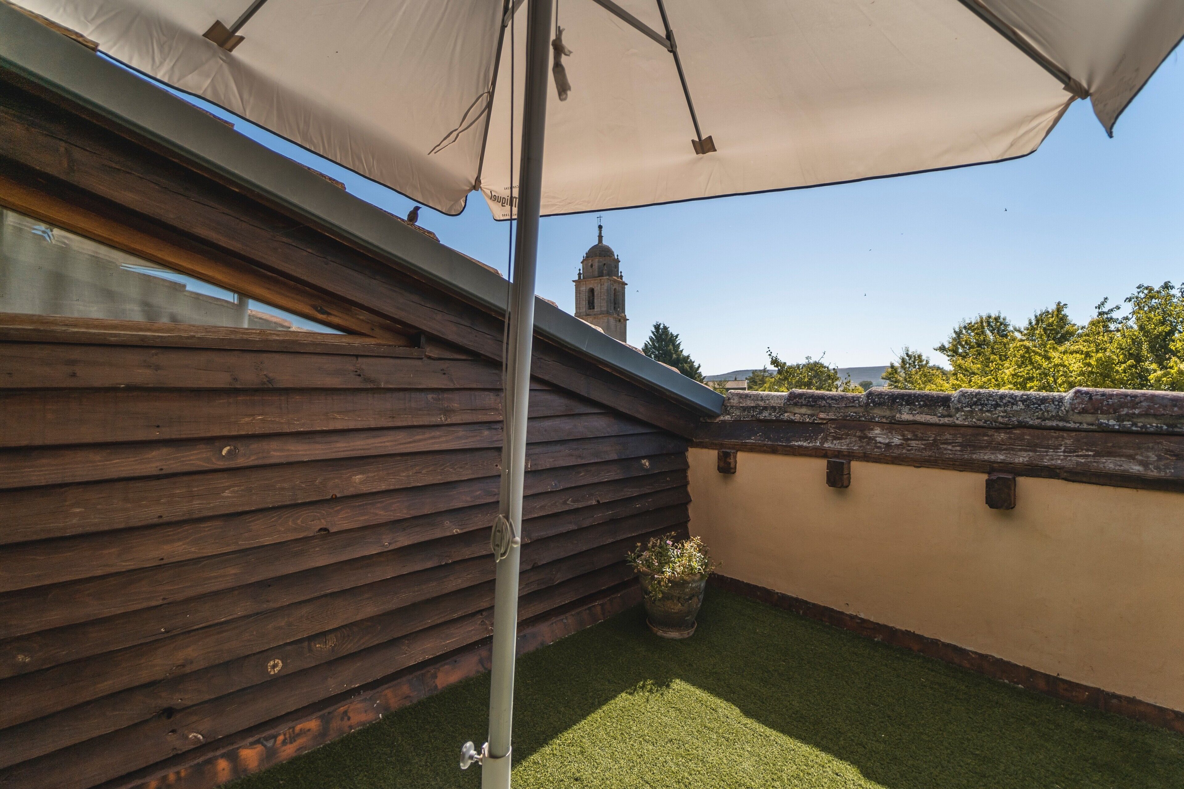 Ett trädäck med en pergola, en krukväxt och utsikt över ett klocktorn.