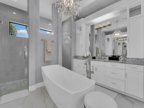 A modern bathroom with a freestanding bathtub, a large mirror, and a chandelier.