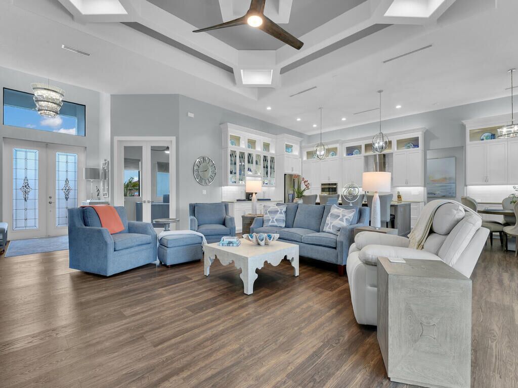 A spacious living room with a high ceiling, large windows, and a modern chandelier.