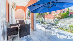 Un espace extérieur aménagé, abrité et doté de meubles en osier et d’un parasol bleu.