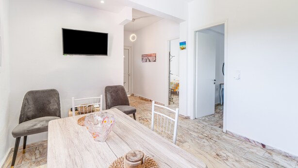 Un coin repas avec une table en bois, deux chaises, un téléviseur fixé au mur et un couloir menant à une autre pièce.