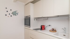 Una cocina con armarios blancos, un microondas, una cafetera roja y un lavamanos pequeño.
