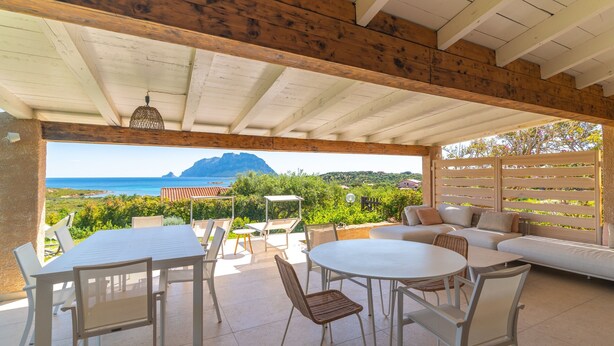 Un patio al aire libre con una mesa y sillas blancas, un sofá y vistas al mar y las montañas.