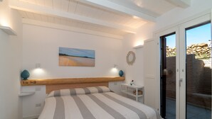 Un dormitorio con cama, una mesita de noche, una lámpara de pared, un cuadro y una puerta corrediza de vidrio que da a un espacio exterior.